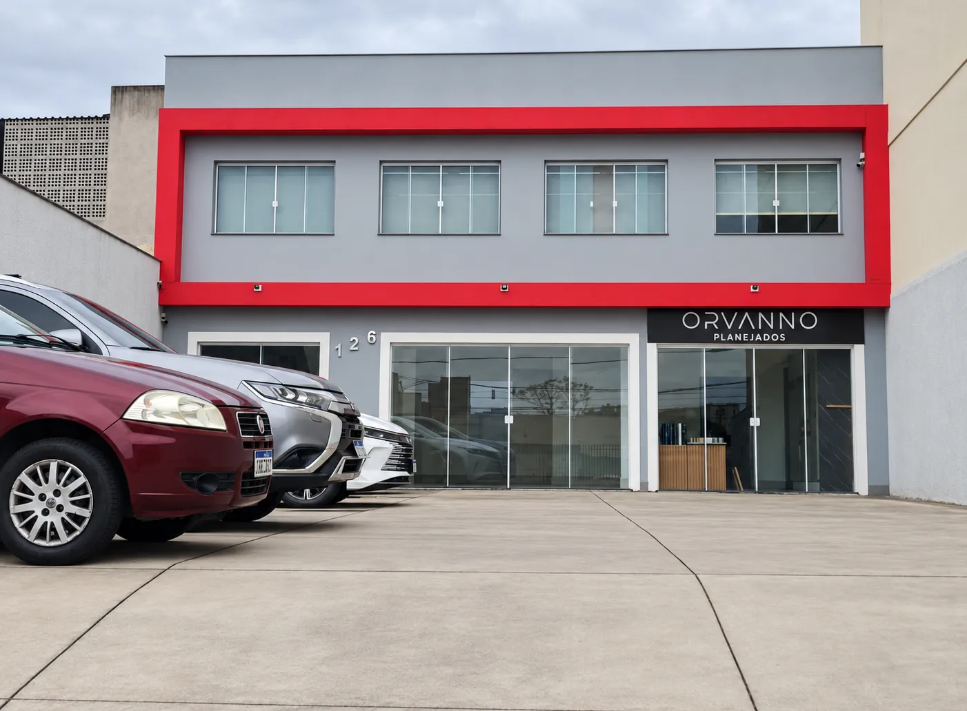Prédio da loja e showroom Orvanno Planejados, com a faixa vermelha, o número 126 e carros no estacionamento em frente.